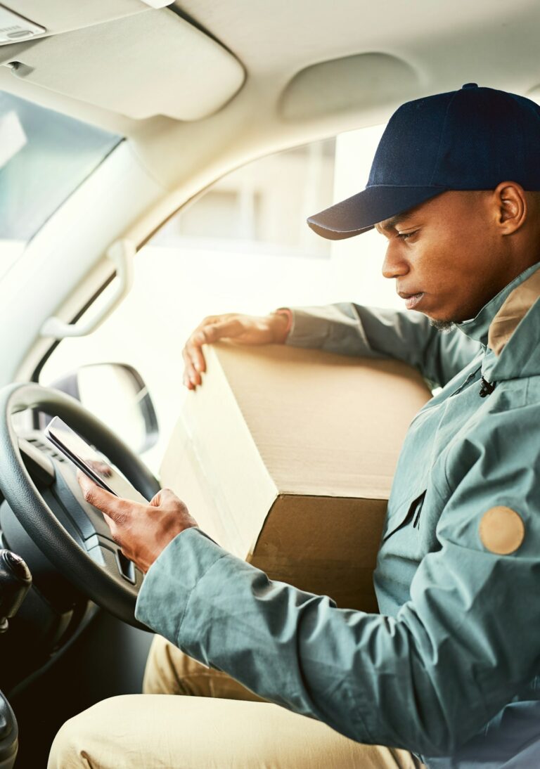 Shot of a courier using a cellphone while sitting in a delivery van