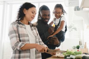 Mother cooking vegetable salad while father and daughter helping her at home kitchen